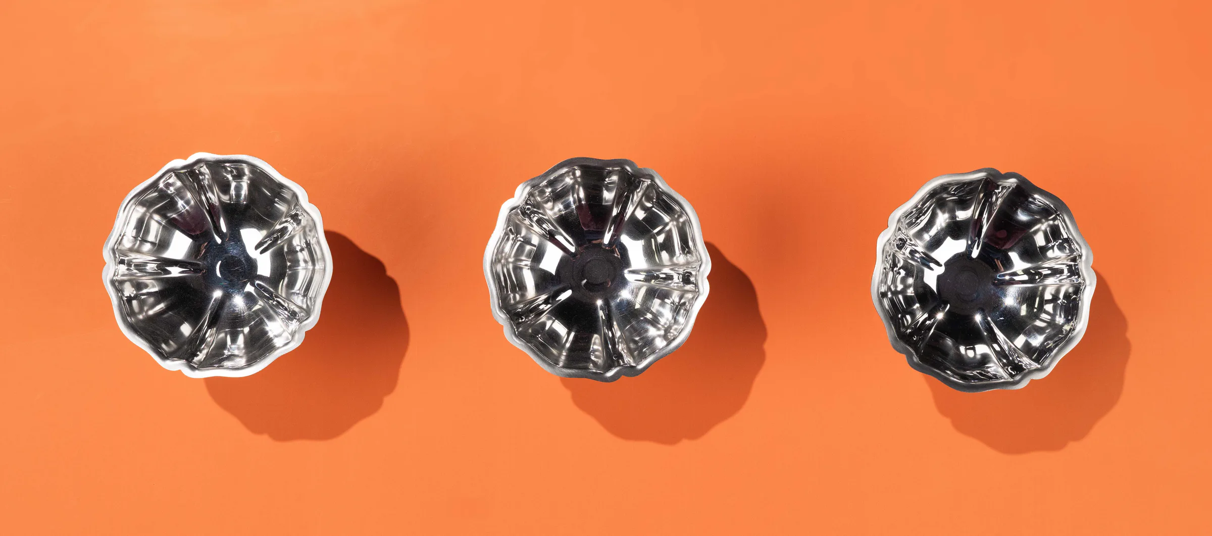 Three silver candy dishes on orange, from above